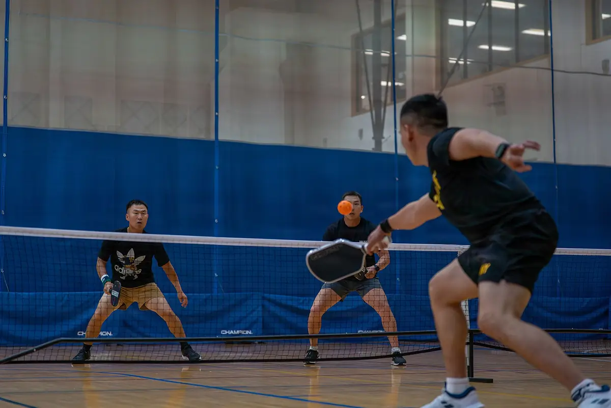 Người chơi pickleball đánh đôi sát lưới trong nhà thi đấu